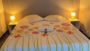 Un lit recouvert d’une couvre-lit à motifs floraux, deux lampes de chevet et une serviette pliée posée sur le lit.