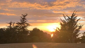 Une vue sur le coucher de soleil, prise depuis une table avec deux chaises, donnant sur un champ verdoyant et des arbres.