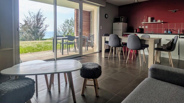Une cuisine moderne avec un mur d’accent rouge, un coin repas offrant une vue sur l’extérieur et une porte-fenêtre coulissante donnant sur une terrasse.