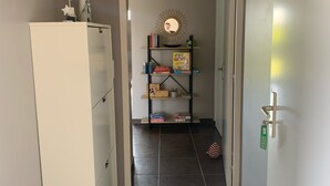 Un couloir avec une armoire blanche, une étagère remplie de livres et un miroir, ainsi qu'un sol carrelé.