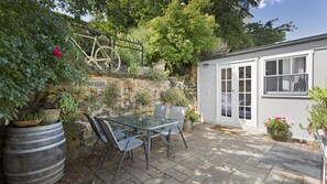 A patio with a table and chairs, a stone wall, and a small shed with a window. - Bluestone Cottage Launceston ITAS (Launceston)