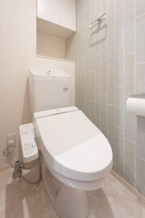 A modern bathroom with a white toilet, a control panel, and a tiled wall. - BEANS STAY Ishibiki (Kanazawa)