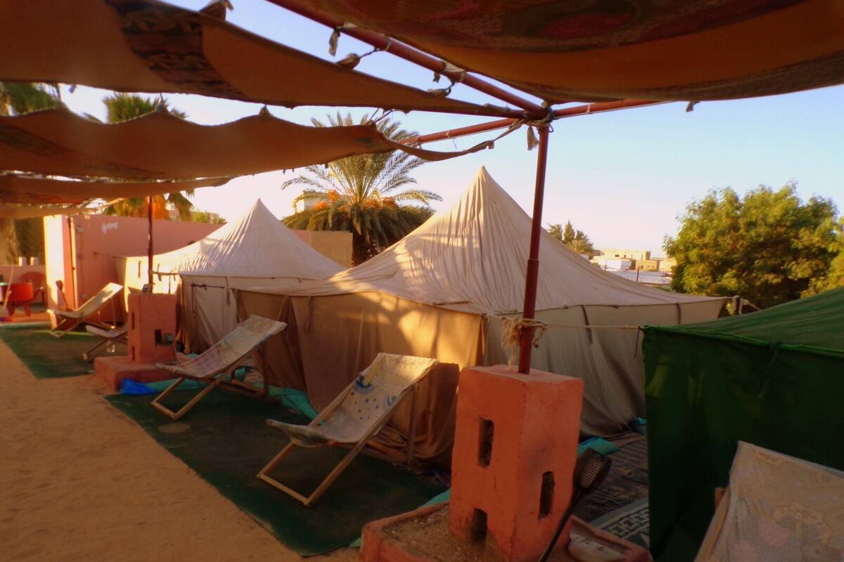 A beachside setup with tents, lounge chairs, and a small structure with a chimney.