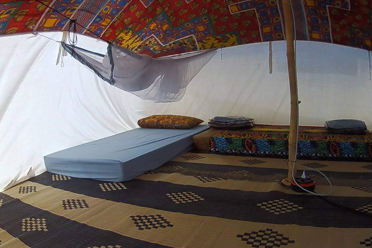 A tent with a blue sleeping area, a patterned rug, and a colorful wall hanging.