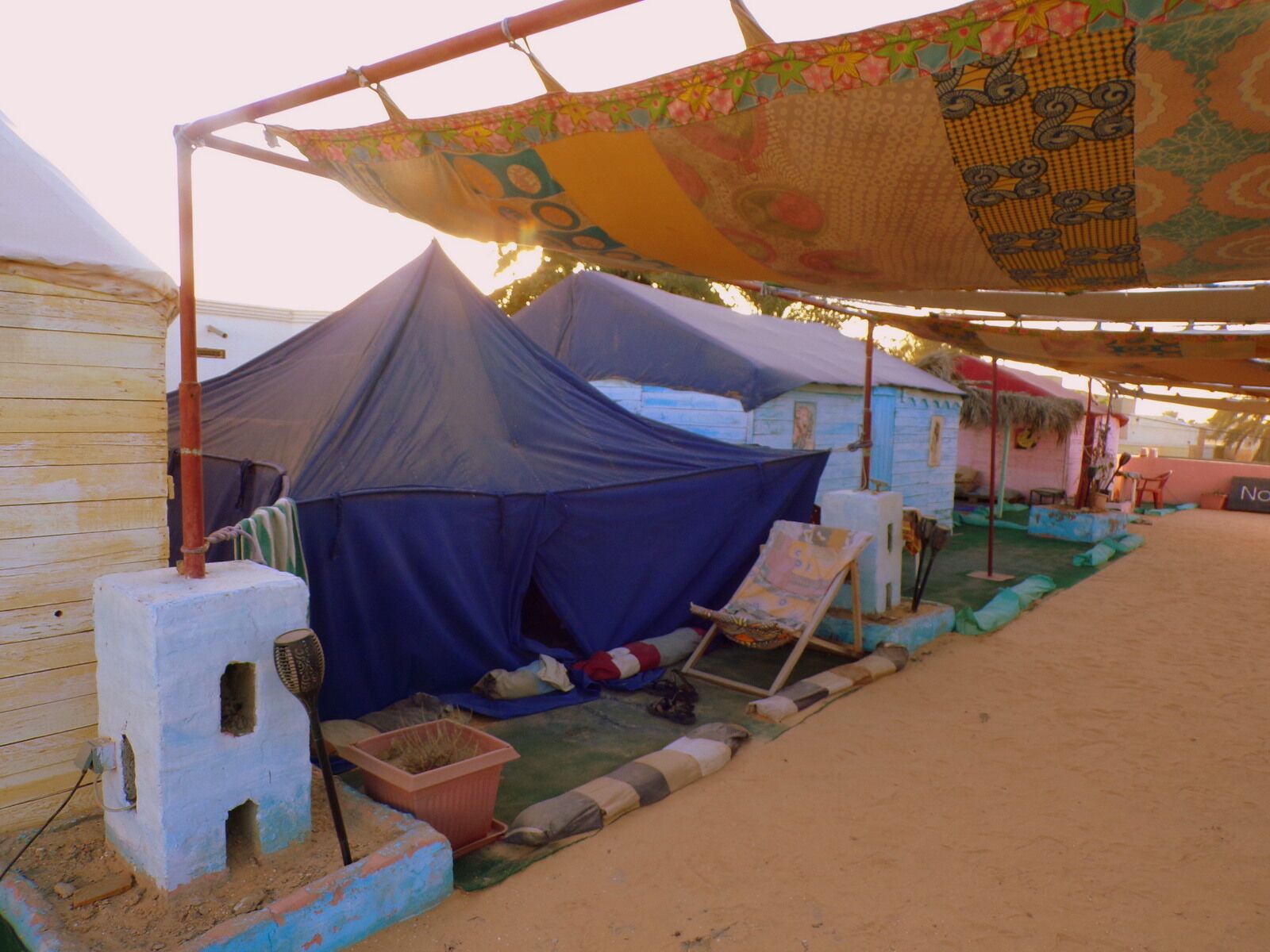 A campsite with tents, a table, and a small structure with a sign.