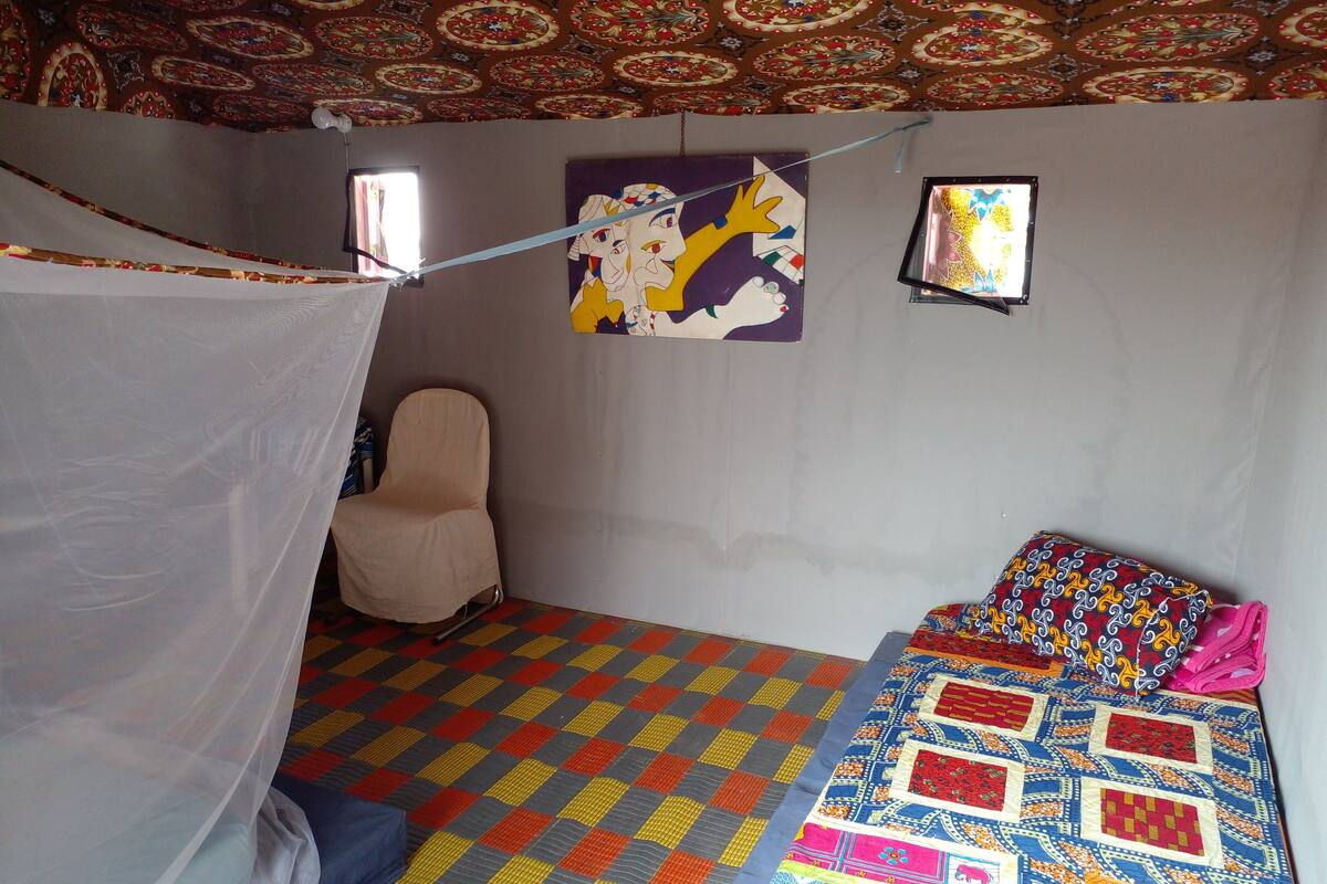 A room with a bed, a chair, a mosquito net, and patterned walls.