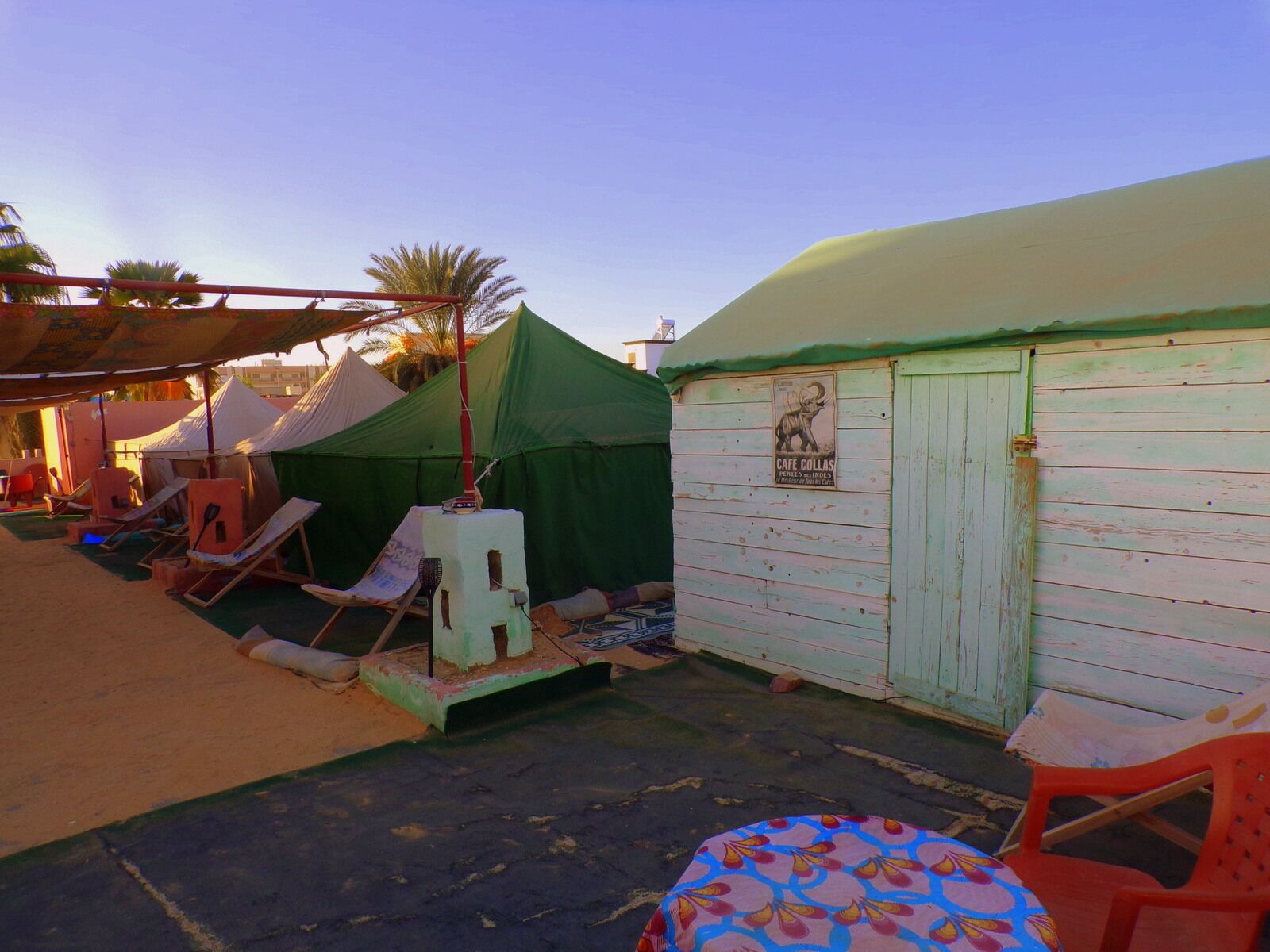 A beachside area with tents, lounge chairs, and a small building with a sign.