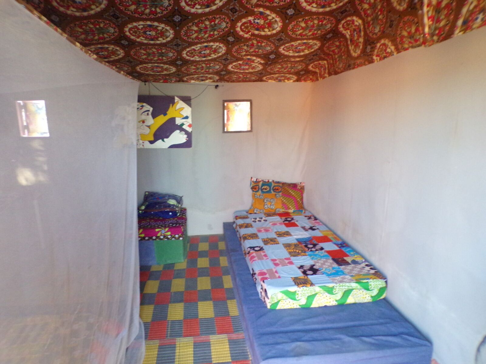 Une petite pièce fermée, avec un plafond décoré de motifs, un sol à carreaux colorés et deux lits recouverts de courtepointes.