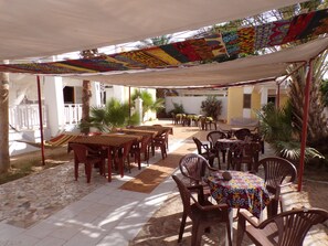 An outdoor patio with wooden tables and chairs, covered by a colorful canopy. - Le Triskell Auberge - Hostel (Nouakchott)