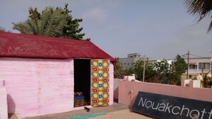 A pink building with a red roof, a colorful door, and a sign reading "Nouakchott". - Le Triskell Auberge - Hostel (Nouakchott)