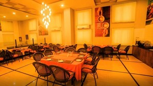 Un comedor con varias mesas y sillas, un candelabro y un ventanal con persianas.