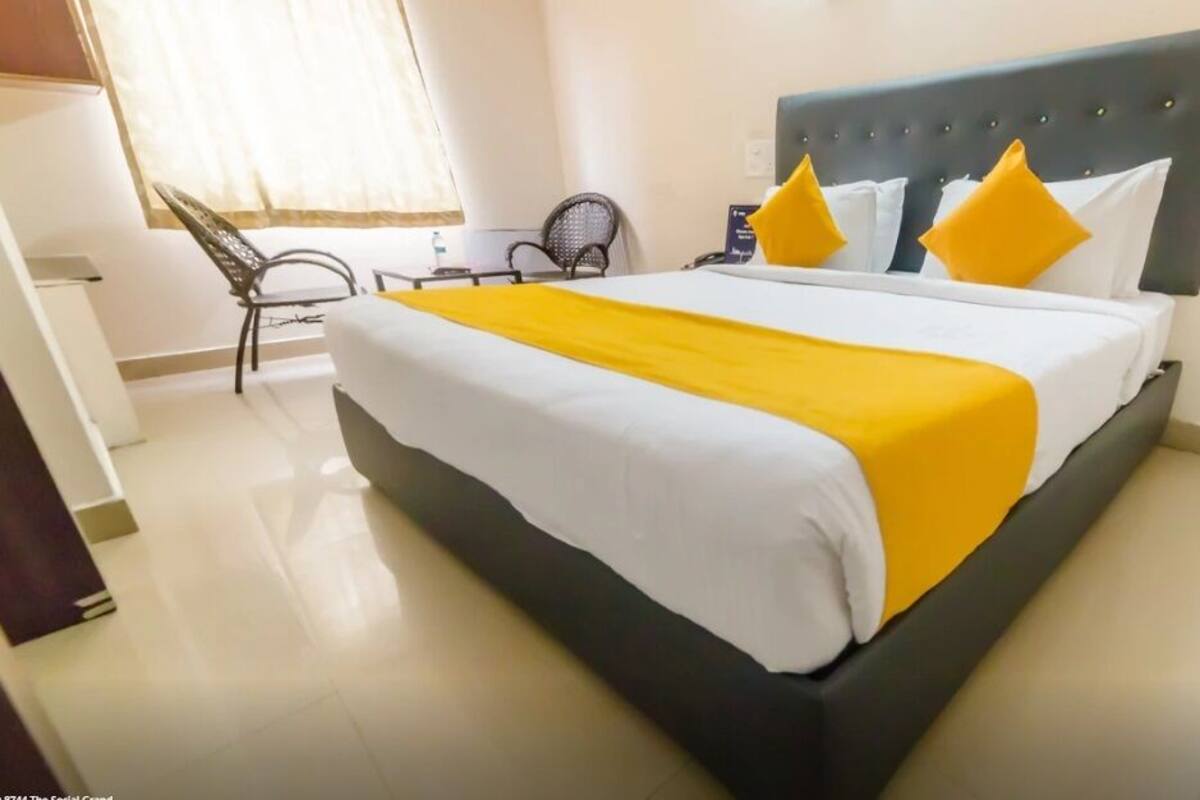 Una cama bien hecha con una colcha blanca y amarilla, un cabecero oscuro y dos almohadas amarillas.