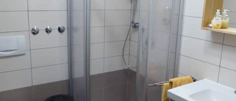 Un baño con ducha separada por vidrio, inodoro, lavamanos y espejo sobre el lavamanos.