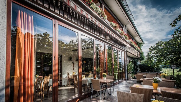 An outdoor patio with wicker furniture, a checkered floor, and a view of the interior through large glass doors. - Landhotel Rebstock (Oberkirch)