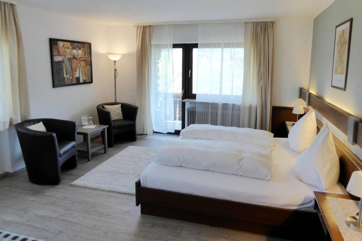 A hotel room with a large bed, a chair, a desk, and a window with curtains.