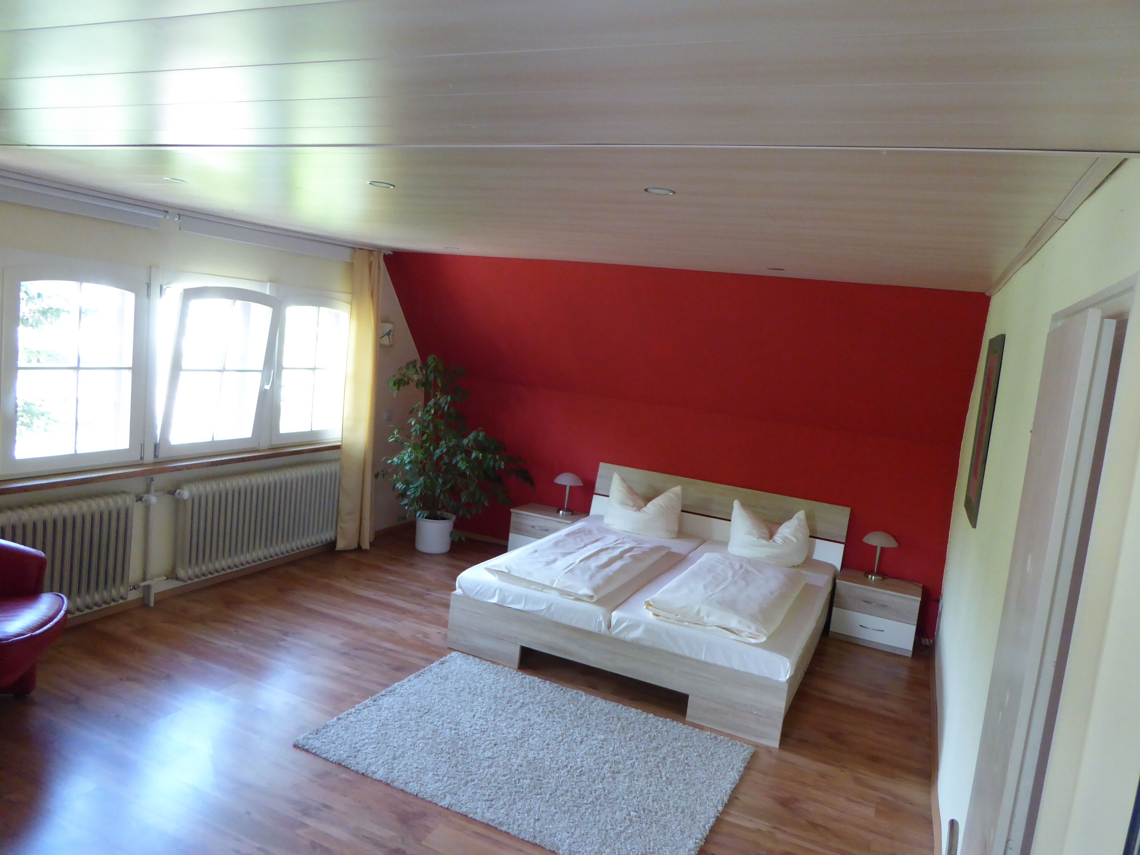 A bedroom with a wooden bed, a potted plant, a radiator, and a window with curtains.