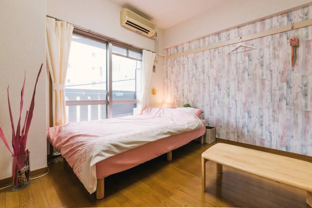 Un dormitorio con una cama, un banco, una planta en maceta y una ventana con cortinas.