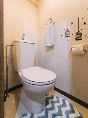 Un baño pequeño con inodoro, una toalla colgada en un perchero y un dispensador de papel higiénico.