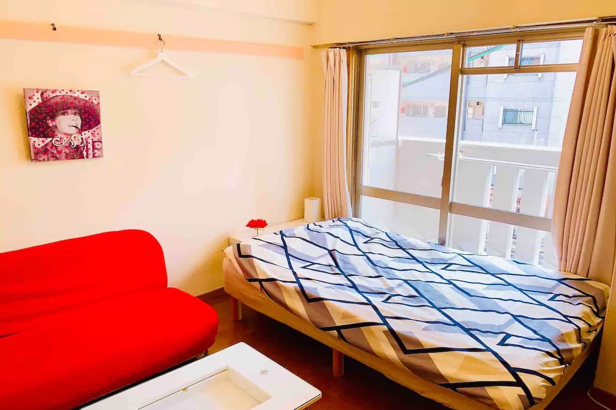 Una habitación con una cama, un sofá rojo y una pequeña mesa.