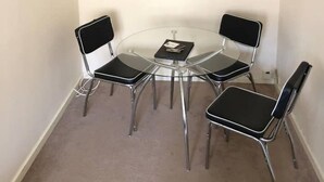 Une petite pièce moderne avec une table en verre et quatre chaises noires, un seul luminaire suspendu et deux œuvres d’art murales.