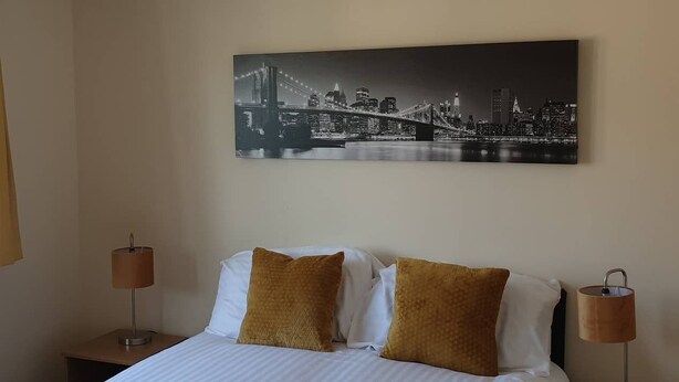 Une chambre d’hôtel avec un lit, deux tables de chevet, deux lampes et un tableau représentant un paysage urbain accroché au mur.
