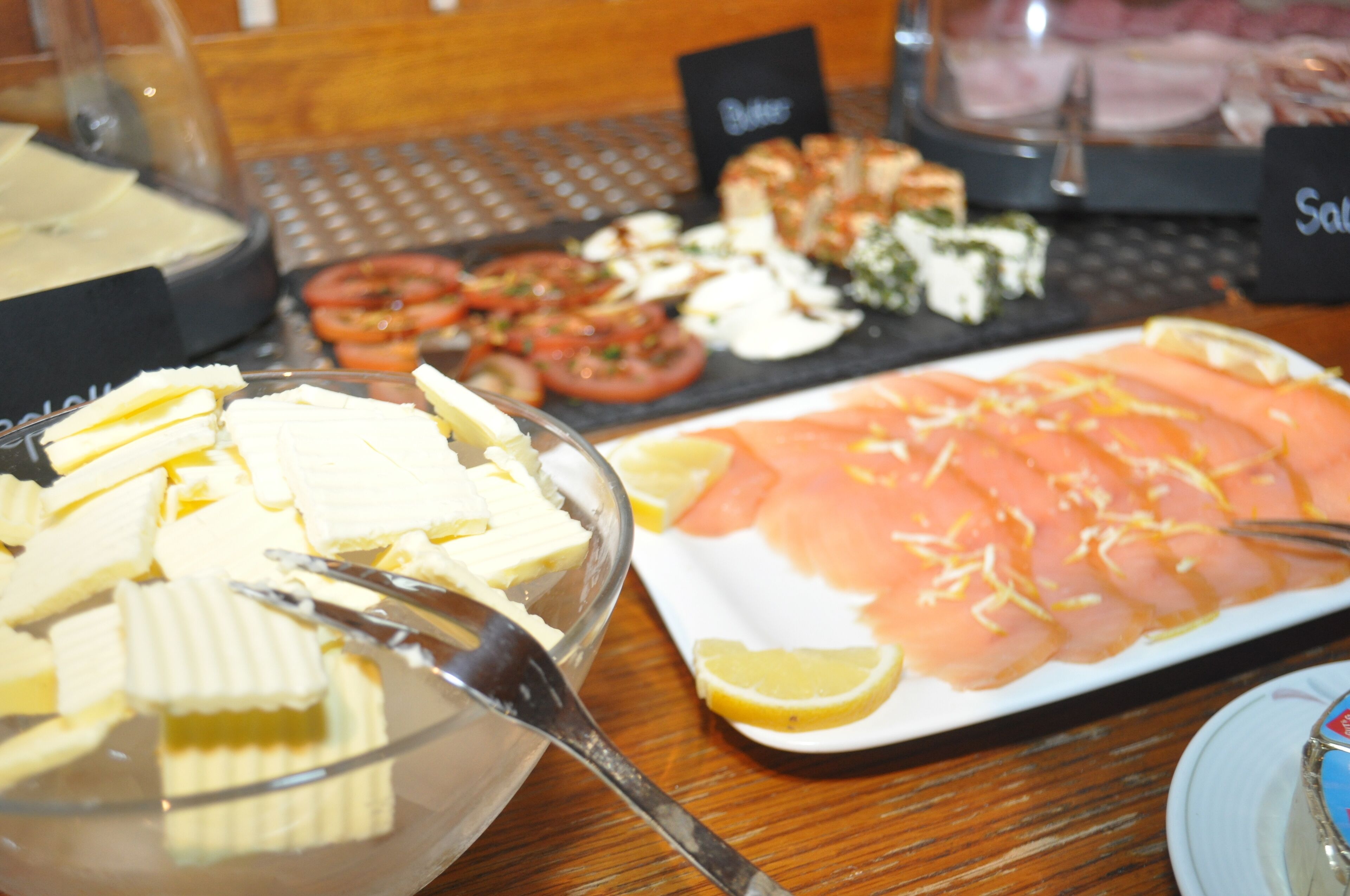 A buffet table with various food items including sliced tomatoes, cheese, and salmon.