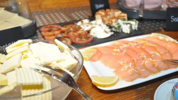 A buffet table with various food items including sliced tomatoes, cheese, and salmon.