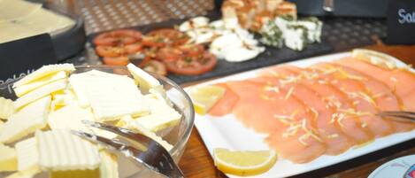A buffet table with various food items including sliced tomatoes, cheese, and salmon.