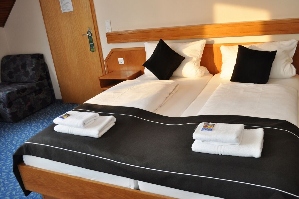 Ein Hotelzimmer mit einem Bett, zwei Kissen, einem Nachttisch, einem Stuhl und einer Tür.