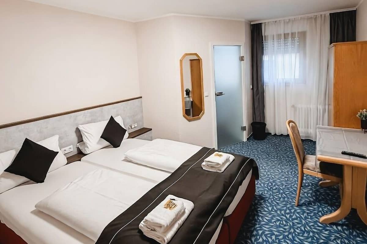 Une chambre d’hôtel avec un lit, un bureau, une chaise, un miroir et une porte.