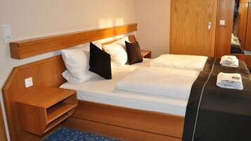 A hotel room with a wooden headboard, a bed with white bedding, a blue patterned rug, and a wooden nightstand.