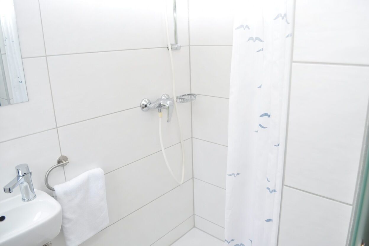Un baño con lavamanos blanco, un espejo, una toalla y cortina de ducha.
