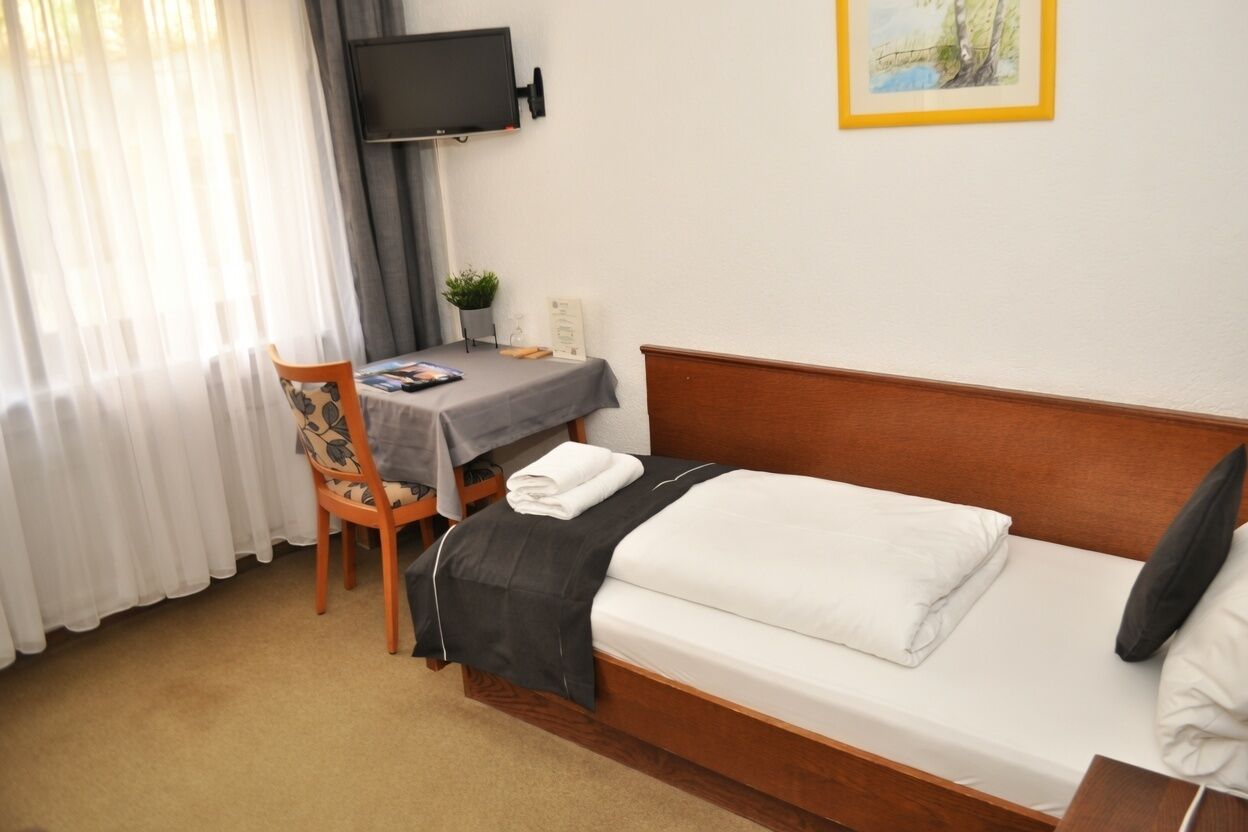 Habitación de hotel con cama, escritorio, silla, televisor y un cuadro en la pared.