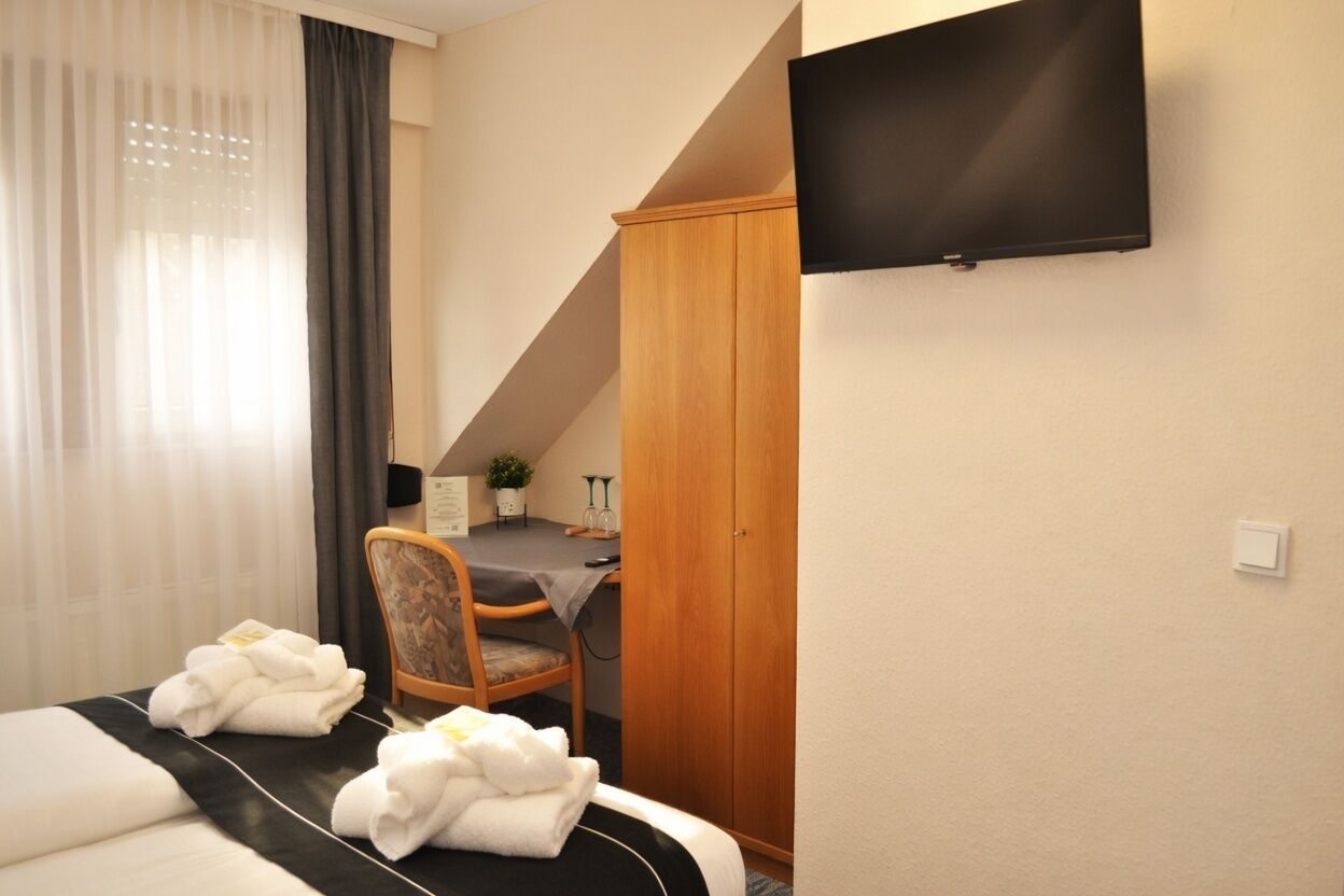 Habitación de hotel con cama, escritorio, silla, armario y televisor.