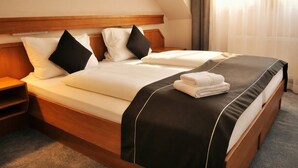 Habitación de hotel con cama doble, dos almohadas, mesita de noche y ventana con cortinas.