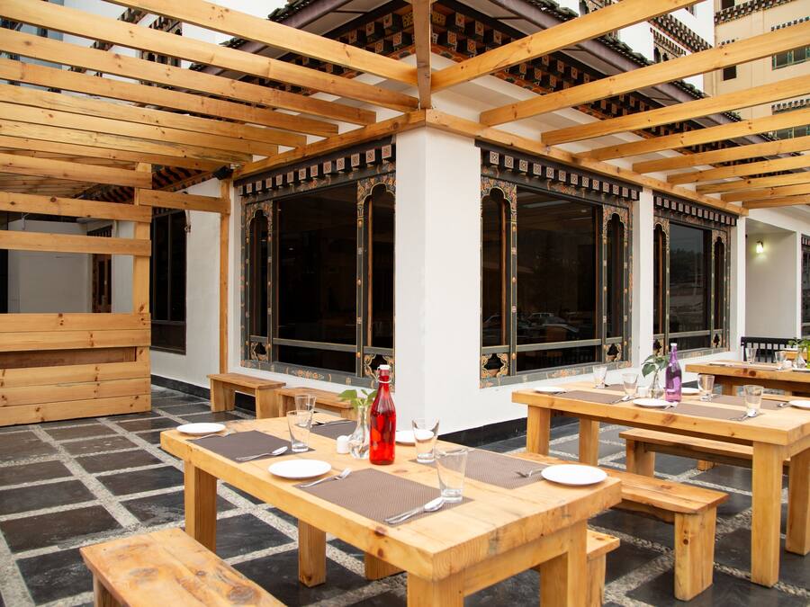 Un espace de restauration en plein air avec des tables et des bancs en bois, de grandes fenêtres et un style architectural traditionnel.