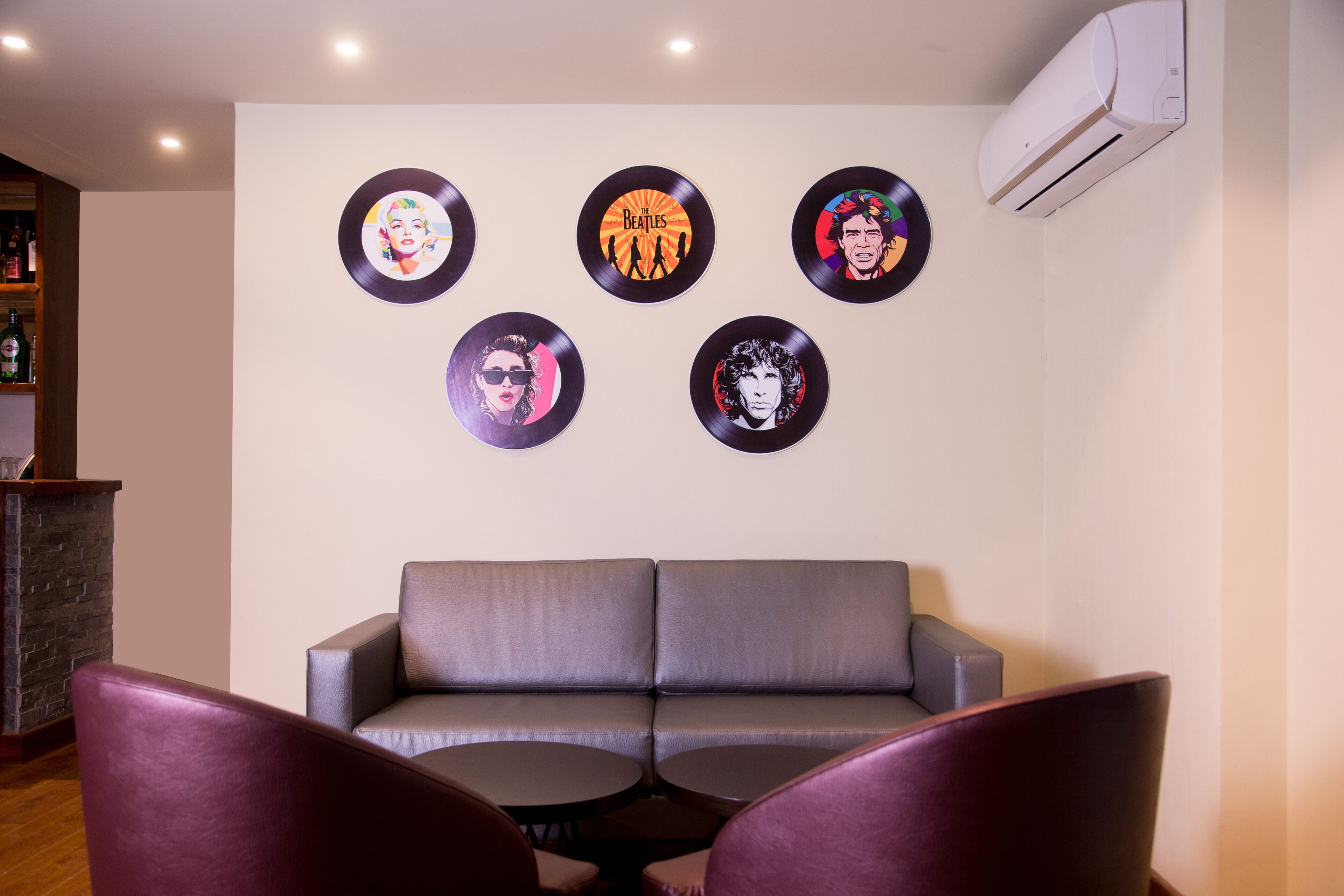 A living room with a grey sofa, two round tables, and five vinyl records on the wall.
