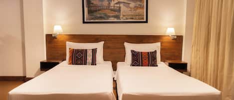 A hotel room with two beds, a wooden headboard, a painting of a bridge, and two bedside lamps.