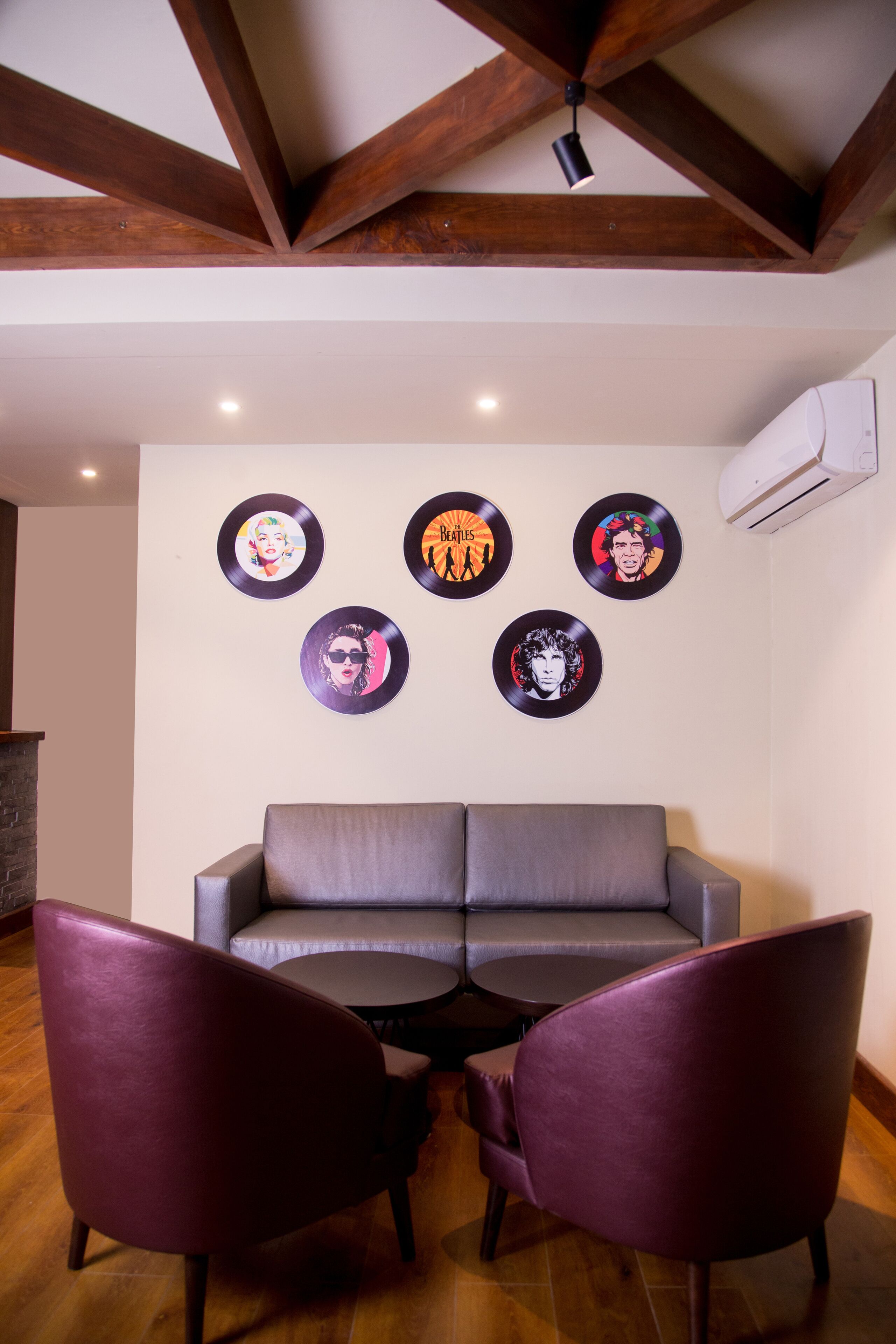 Un salon moderne avec un canapé gris, deux fauteuils violets et des disques vinyle accrochés au mur.