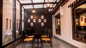 A cozy indoor seating area with a table and chairs, framed artwork on the wall, and a view through large windows. - Lemon Tree Hotel Thimphu (Thimphu)