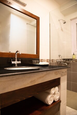 A bathroom with a large mirror, a sink, and a shower. There are towels on a shelf and a soap dispenser on the wall. - Lemon Tree Hotel Thimphu (Thimphu)