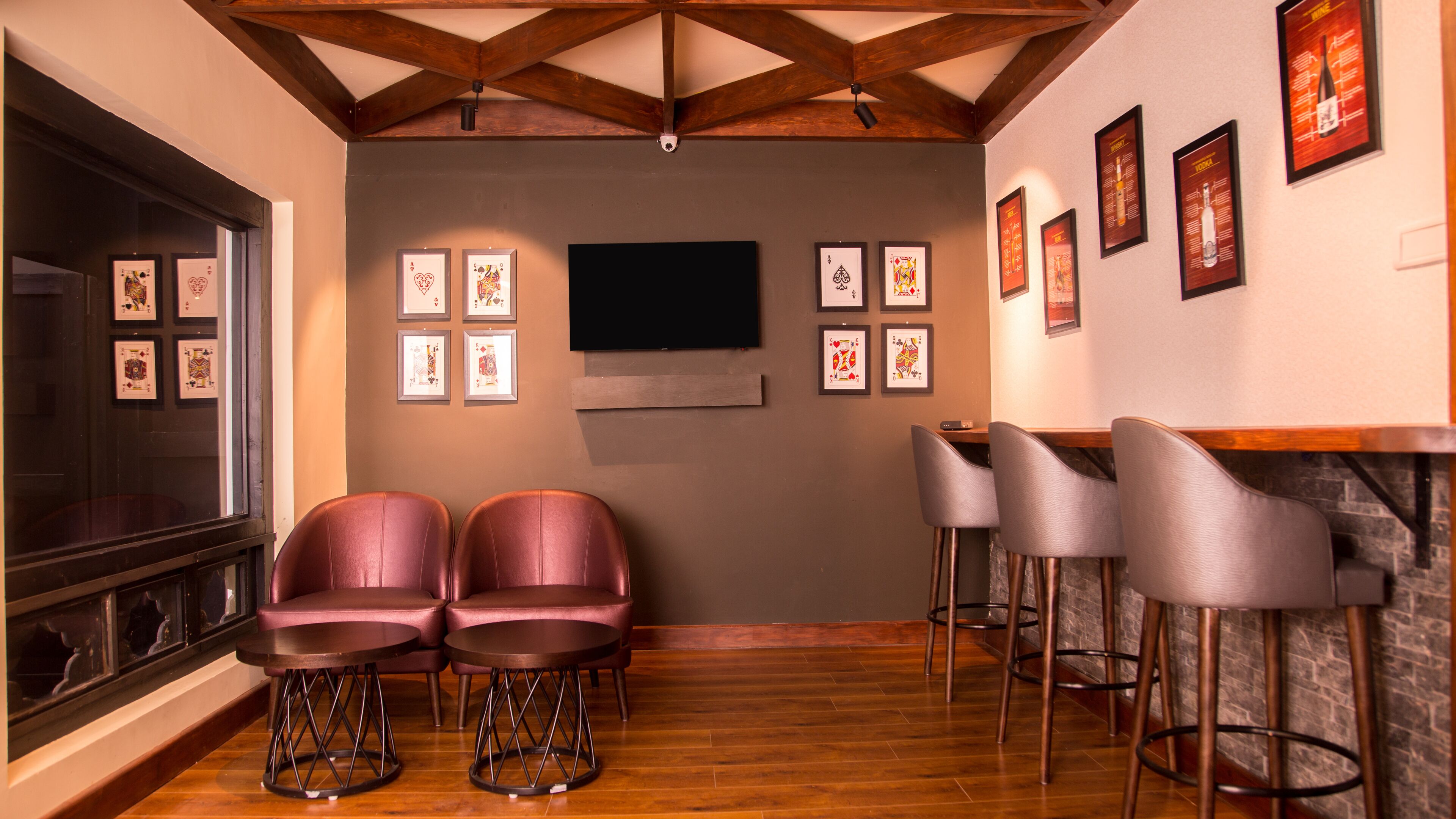 A bar area with two cushioned barstools, a flat-screen TV mounted on the wall, and framed pictures on the wall.
