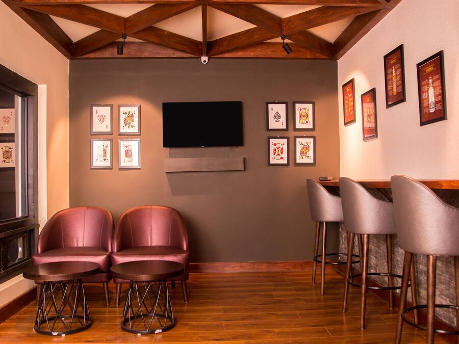 A bar area with two cushioned barstools, a flat-screen TV mounted on the wall, and framed pictures on the wall.
