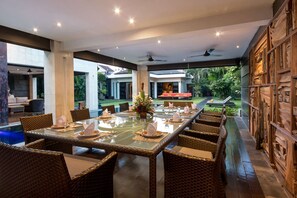 A spacious dining area with a long table, wicker chairs, and a view of a lush garden and pool. - Beautiful Villa With Private Pool, Bali Villa 2001 (Seminyak)