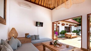 A modern living room with a sofa, a coffee table, and a TV. There is a wicker lamp and a basket on the floor. - Villa for Rent in Bali 2046 (Seminyak)