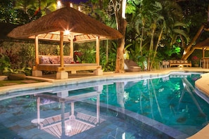 A poolside area with a thatched gazebo, lounge chairs, and a seating area with cushions.
