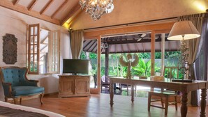 Une pièce spacieuse avec un grand lit, une télévision, un bureau en bois et une vue sur une végétation luxuriante.