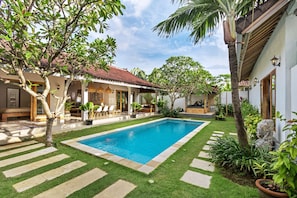 Zona de piscina con piscina, área de estar techada y un pequeño jardín.