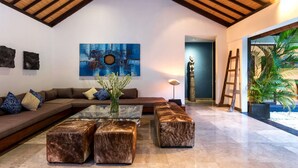 A modern living room with a high ceiling, a large abstract painting, a sofa set, a glass coffee table, and a potted plant. - Bali Villa Near the Beach, 2080 (Seminyak)
