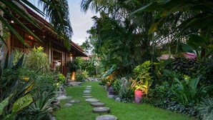 A garden pathway with stepping stones leading to a wooden building with a thatched roof.